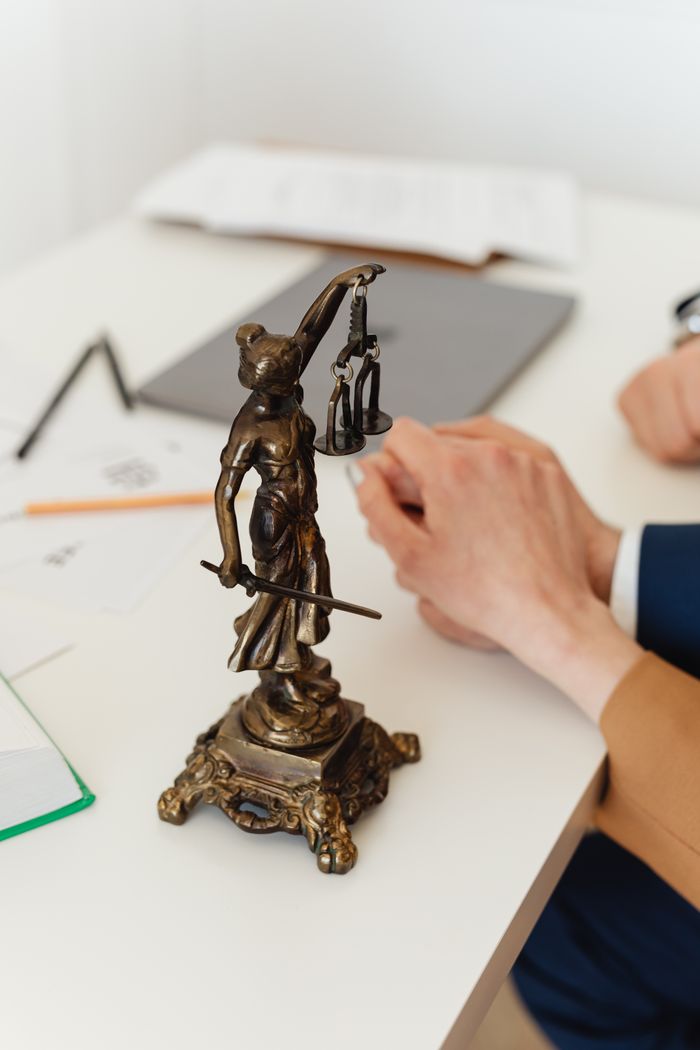 Services Bronze Lady Justice statue on a white office desk with hands in the background. Symbol of law and fairness.
